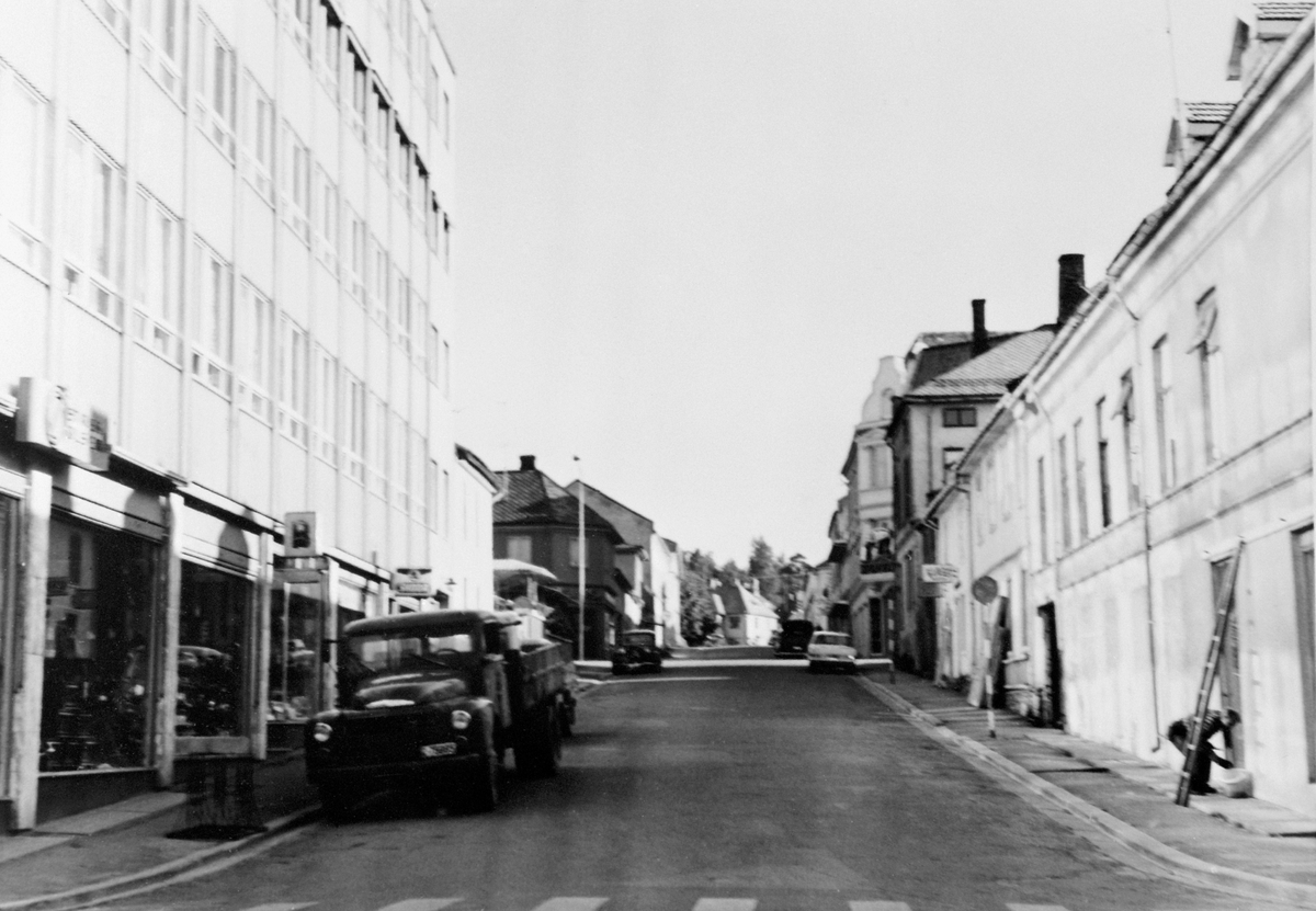 Anno Domkirkeodden, OVERSIKT BEKKEGATA SETT FRA STRANDGATA, PARKERT LASTEBIL VED CASA BLANCA, MANN MALER VEGGEN HOS LAGERET TIL SVARE & BERG