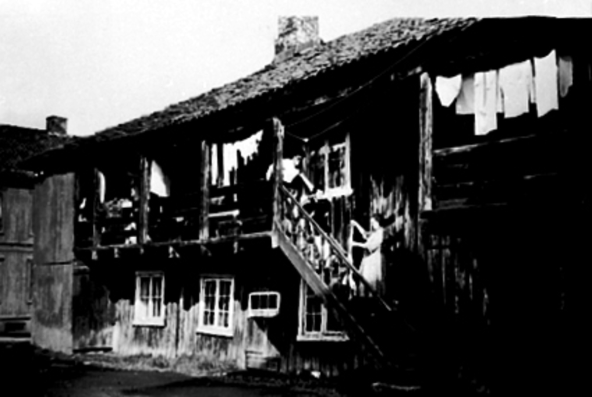 Anno Domkirkeodden, Korslundgården,Torggata 104, Hamar. Klesvask, Klara Solheim henger opp tøy på klessnor. Søstrene hennes sitter i trappa. Kjell Arne Kjeldsen står i svalgangen.