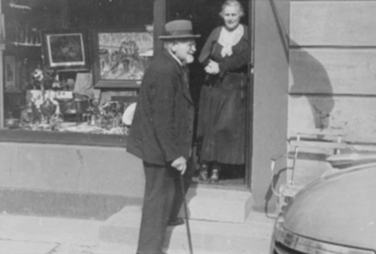 Anno Domkirkeodden, RAGNA PRAG MAGELSEN, STÅENDE I DØRÅPNING PÅ SIN ANTIKVITETSFORRETNING I ENGGATA; HAMAR. HENNES FAR, MATHS PEDERSEN (F. 1843 - D. 1943) GÅENDE UTENFOR MED STOKK, .