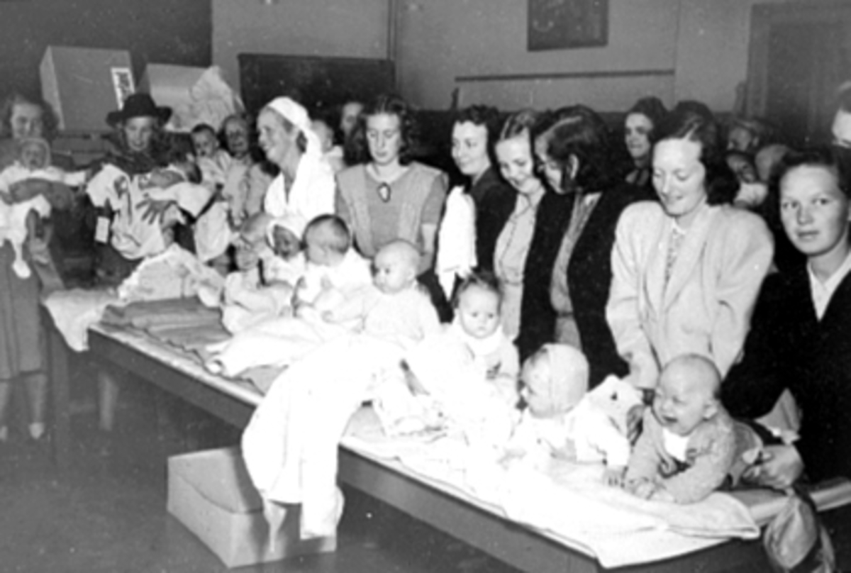 Anno Domkirkeodden, INTERIØR: MIDTBYEN SKOLE, SPEBARNKONTROLL TIL HØYRE BJERKLI, ERNA MED SØNNEN BJERKLI, STEINAR, STOR GRUPPE MED MØDRE OG SMÅ BABYER.