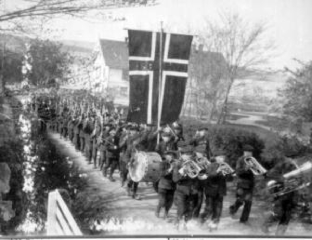 Anno Domkirkeodden, 17. mai-toget marsjerer over tunet på Toftes Gave, Nedre Sund, Helgøya med orkester i front. Mange mennesker og flagg.