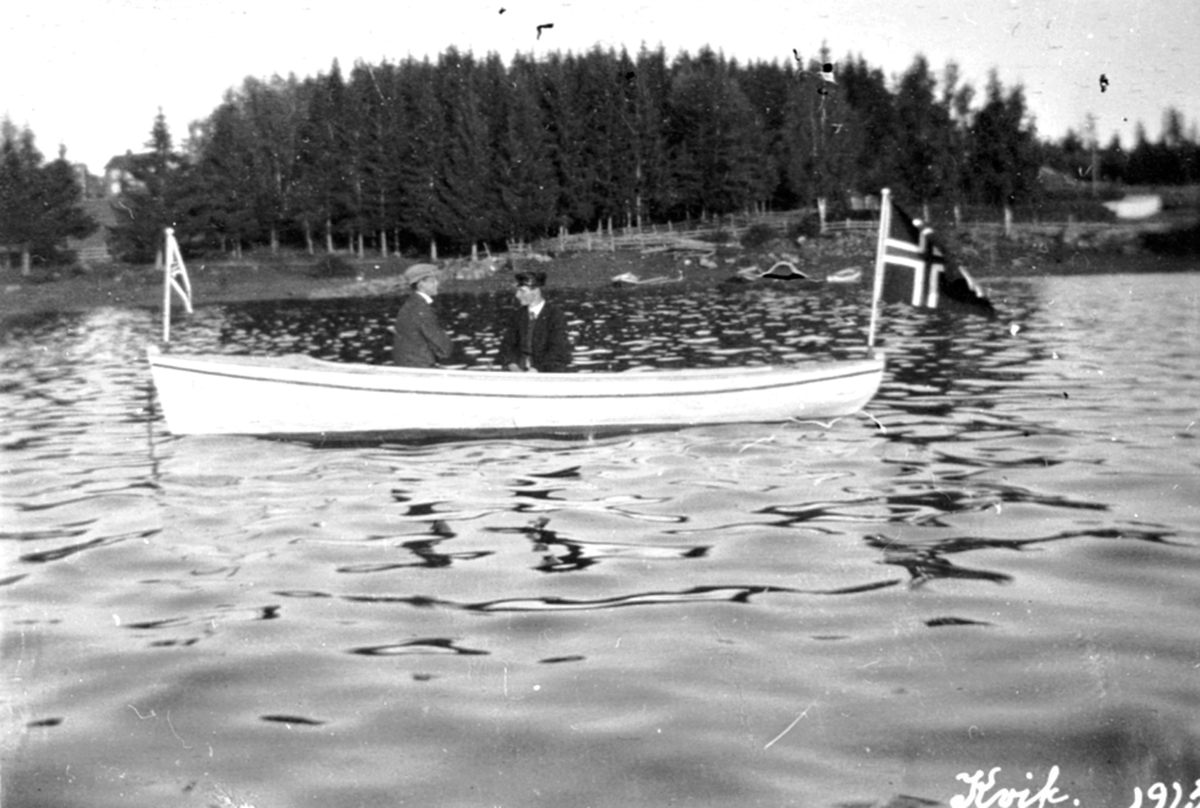 Anno Domkirkeodden, To menn i motorbåten "Kvik", Brumunddal. Vimpel foran og flagg bak.