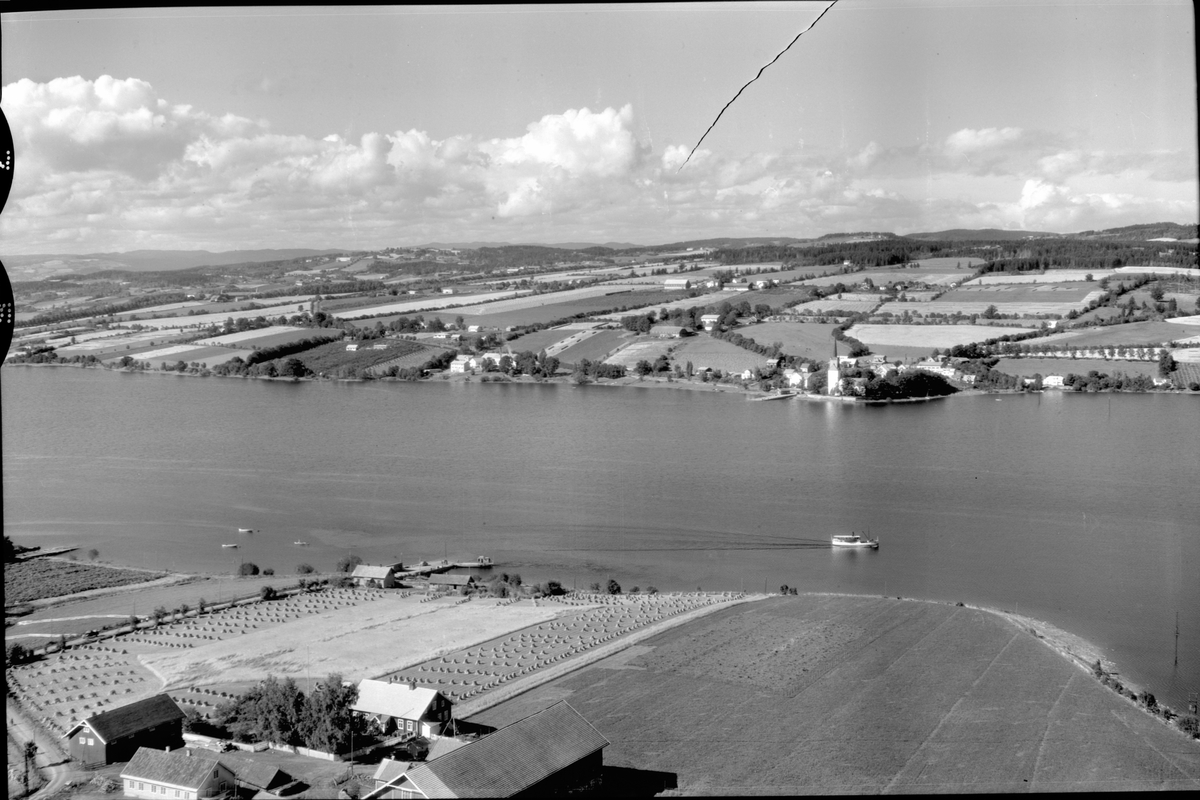 Anno Domkirkeodden, Flyfoto, landskap, Helgøya, Nessundet, Mjøsa, Tingnes i bakgrunn, Nes kirke. Mjøsbåten i Nessundet er trolig M.S. Kvikk som ble flyttet til Mjøsa i 1925 og overtatt av Nes Damskibselskap i 1931.