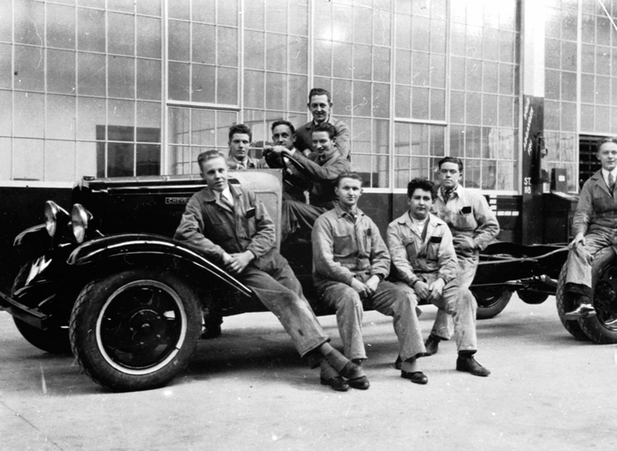 Anno Domkirkeodden, Gruppe menn i kjeledress rundt en Chevrolet 1929-33 modell. Bilmekanikere på kurs. Johannes Haug (1909-1986) fra Nes Bilverksted.