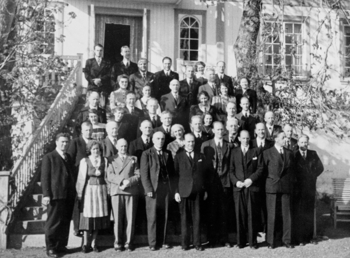 Anno Domkirkeodden, Stor gruppe geistlige, prester på trappa i hovedbygningen på Hovelsrud, Helgøya i Ringsaker, 6. mai 1945. Vertskapet Ragnhild og Karl B. Olssøn i første rekke nr 2 og 3 fv. Forviste prester under krigen, fredsdagene.