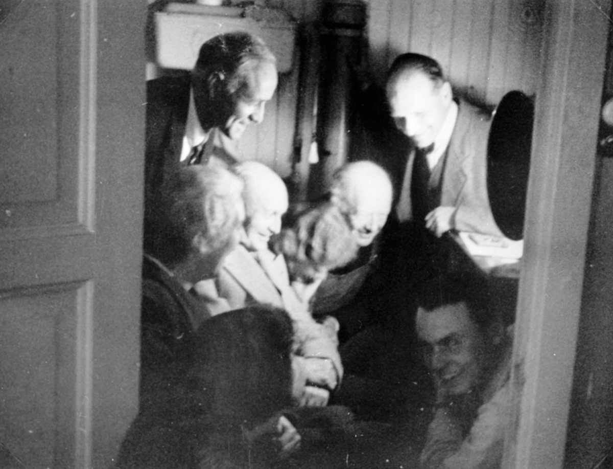 Anno Domkirkeodden, 8 personer samlet på toalettet for å høre nyheter på radio om freden den 7. mai 1945, klokken 15.03. Tilstede var Ragnhild og Carl B. Olssøn, domprost Kobro, Nils Olssøn, biskop Wollert Krohn-Hansen. På Hovelsrud, Helgøya.