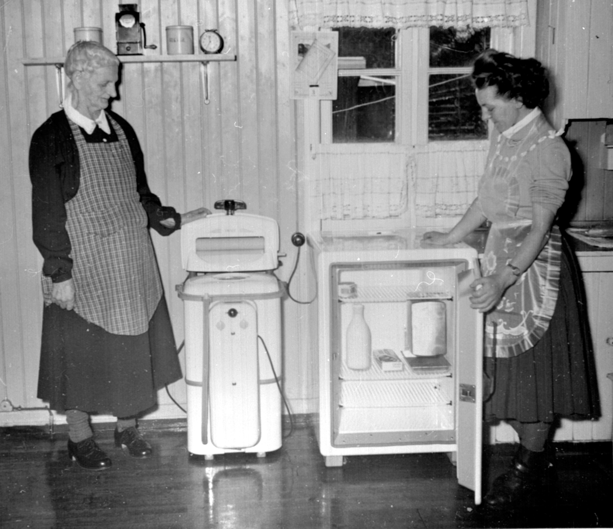 Anno Domkirkeodden, Interiør, kjøkken 2 damer med vaskemaskin og kjøleskap. Berger Langmoen A/S, Brumunddal. Høsten 1954 fikk alle ansatte på Langmoen 500 kroner for å kjøpe seg vaskemaskin. Til venstre er Petra Jevne og Paula Jevne g. Olsen.