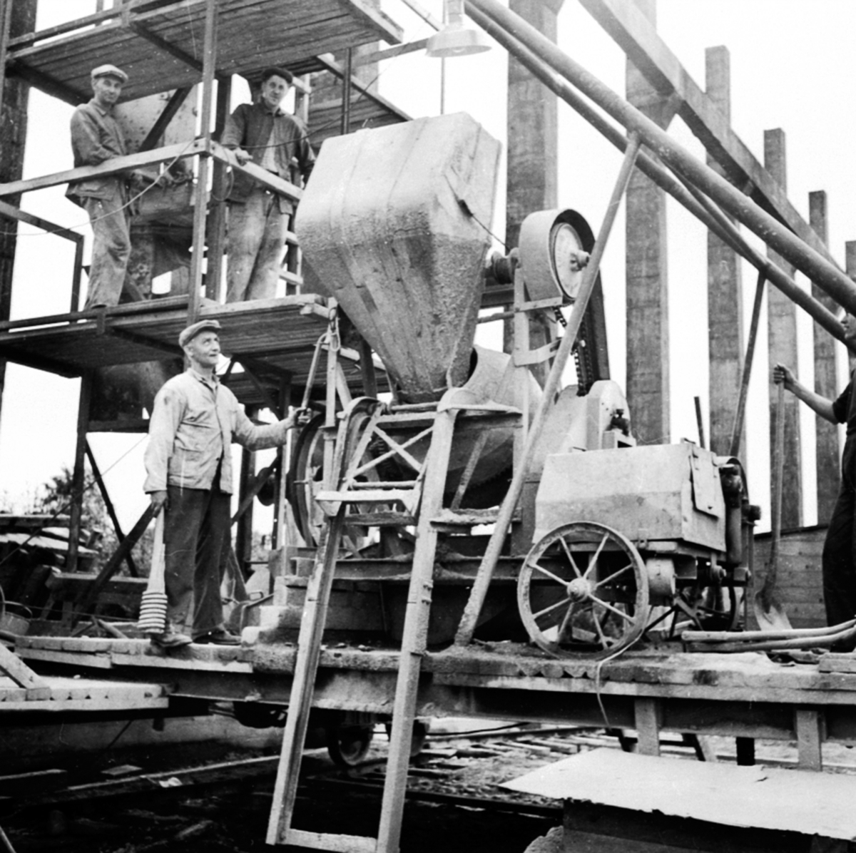 Anno Domkirkeodden, Fundamentering, murerlag blander sement i motorisert sementblander, bygging av nytt materiallager, Berger Langmoen A/S, Brumunddal. Virkesmagasinet under oppførelse, støping, Nederst står Syver Myhr, på plattformen Johannes Romskaug og Ole Halvorsen.