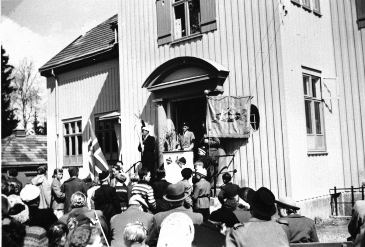 Anno Domkirkeodden, 17. maifeiring på Brumund skole, Brumunddal. Folk samlet foran trappa med flagg og faner. Talerstol i døre.