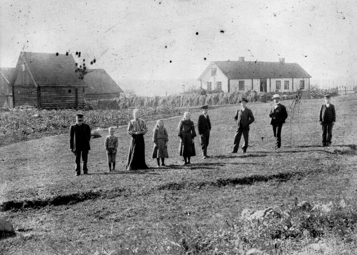 Anno Domkirkeodden, Gruppe personer foran bygninger på Maurud nedre, Helgøya. Lars Larsen Lier (1832-1910), Ottar f.1899, Teoline Torsdatter Fjeld (1853-1929) , Karen Sofie f.1895, Lovise f.1893, Torstein (1888-1971), Leonard (1885-1978), Torolf Hansen Vien f.1879, Magne (1891-1972).