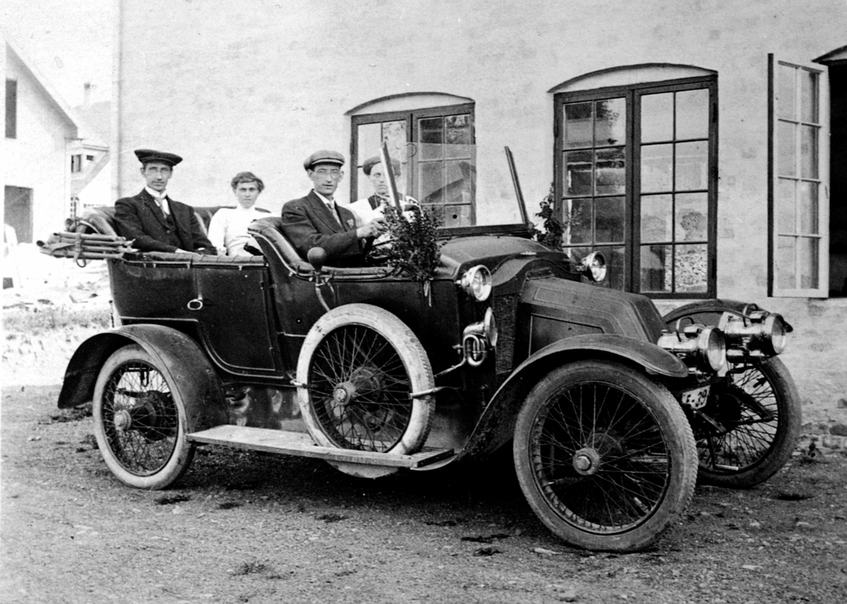 Anno Domkirkeodden, Orginal tekst: Bil, Renault ca. 1910-14 modell. Reg-nr E-39. Passasjerer er fotograf Simen Baardseth, Dagny Baardseth født Ovesen, sjåfør Even Baardseth og Mathea Baardseth. ---- kommentar start ---- Dette er en Renault ca 1911-12. Det kan ikke være Even som kjører. I følge folketellingen av 1910 v…
