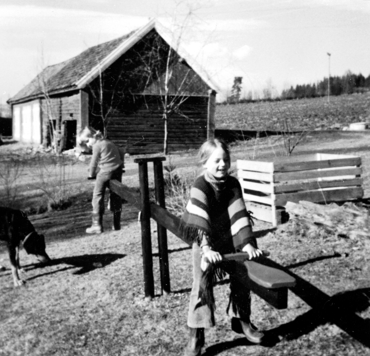 Anno Domkirkeodden, 2 jenter som leker på vippehuske. Grete Tørud f.1966 og Bodil Tørud f.1967. I bakgrunnen er det gamle huset som hadde svalgang. Revet. Skavang, Helgøya.