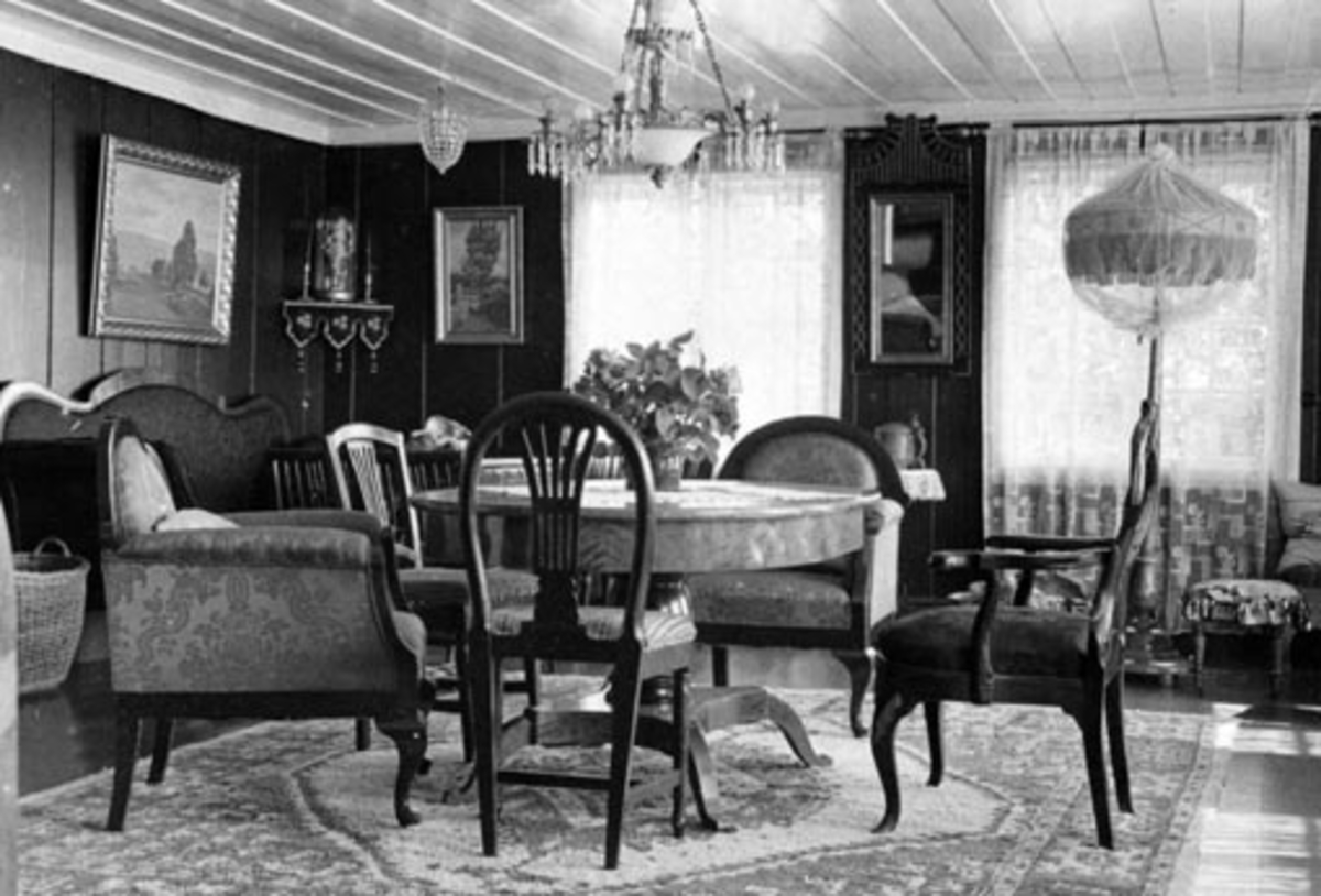 Anno Domkirkeodden, Interiør fra storstua på Ousdal nordre, Nes, Hedmark. Prismelamper, Biedermeier møbler, sofa, lenestoler, gardiner, speil, gulvteppe.