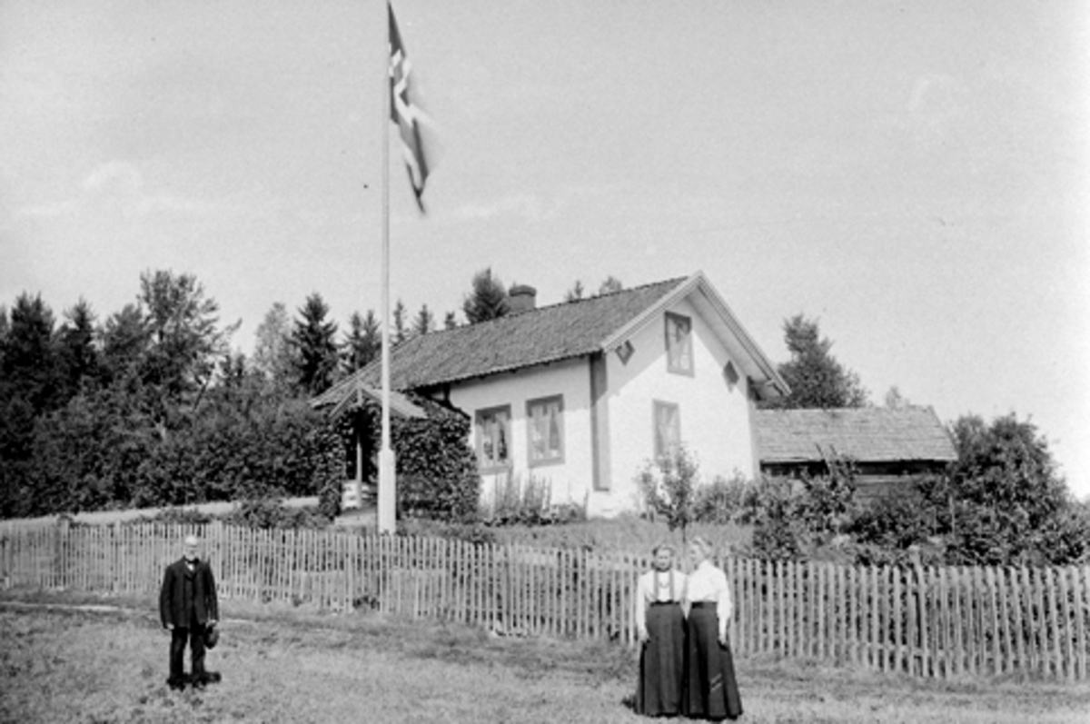 Anno Domkirkeodden, Eksteriør Høiby, Nes, Hedmark. Personene er Gulbrand Olsen Dæhli (1833-1912), Johanne Dæhli (1873-1952), Klara Dæhli (1876-1964). Gudbrand Olsen Dæhlie den første lærer i Dæhli krets. Huset ble flyttet opp fra Kongsrud, revet i 1930. Originalen finnes på glassplate.