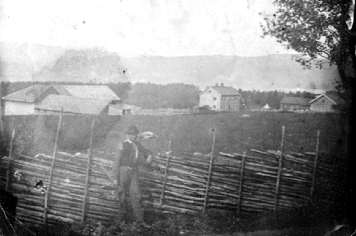 Anno Domkirkeodden, Eksteriør gardsbruk. Helgeby, Nes, Hedmark. Jacob Olsen Lie (1832-1918) i forgrunnen ved skigarden.