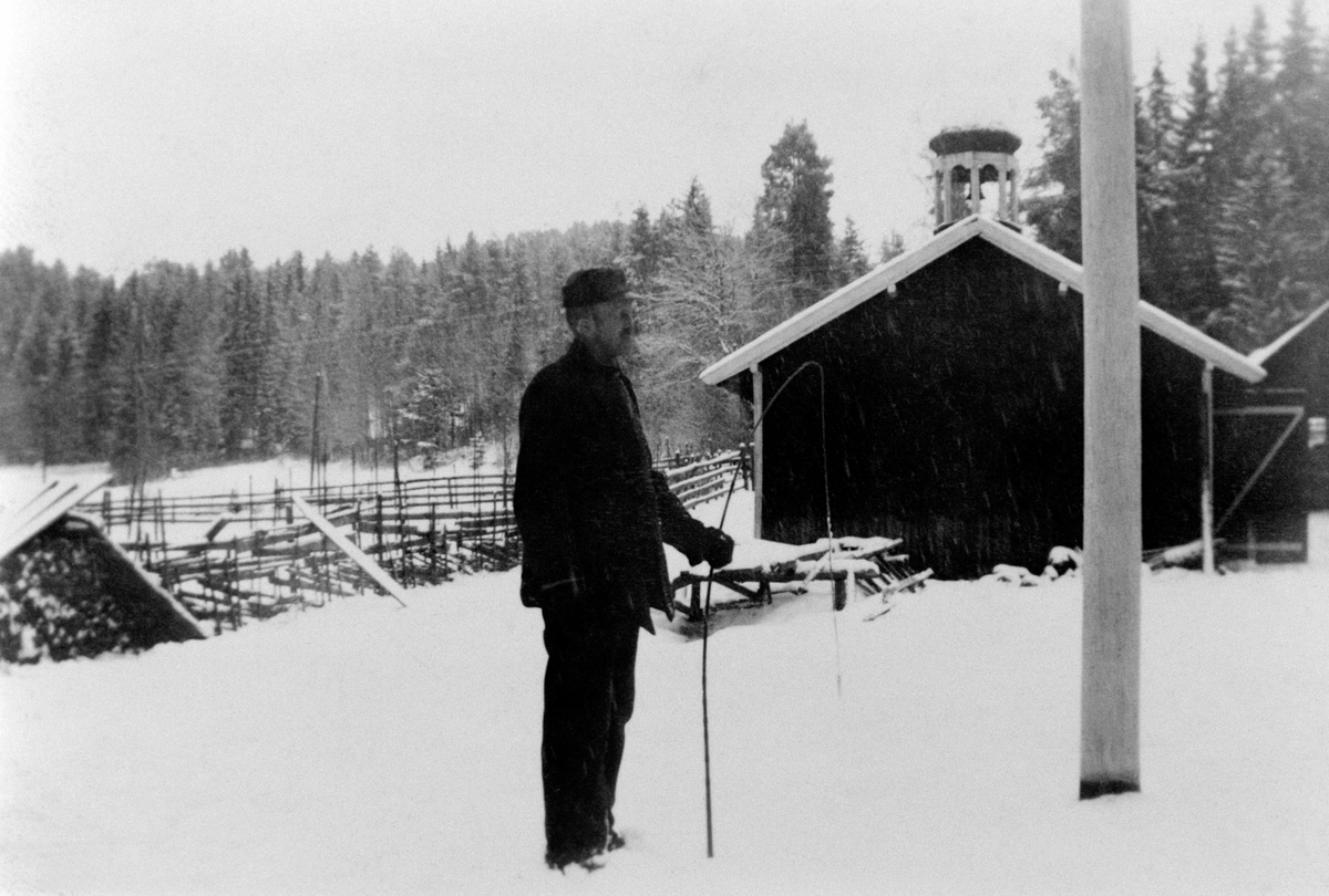Anno Domkirkeodden, Vinter på Sandvold, Nes, Hedmark. Gardstun med vognskjul, saghus i bakrgrunnen. Mannen er Karl Andersen Rosenlund (1902-1955), gardskar som bodde i Sandvollsveen med familien.