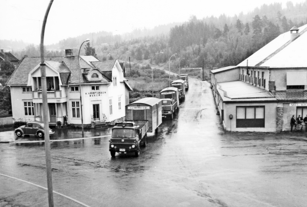Ukjent, Moelv, krysset Storgata, Brugsvegen. Bilkolonne med brakker fra Moelven Brug. Nærmeste lastebil Bedford, modellen kom ny ca. 1960. H. Kristiansen bakeri.