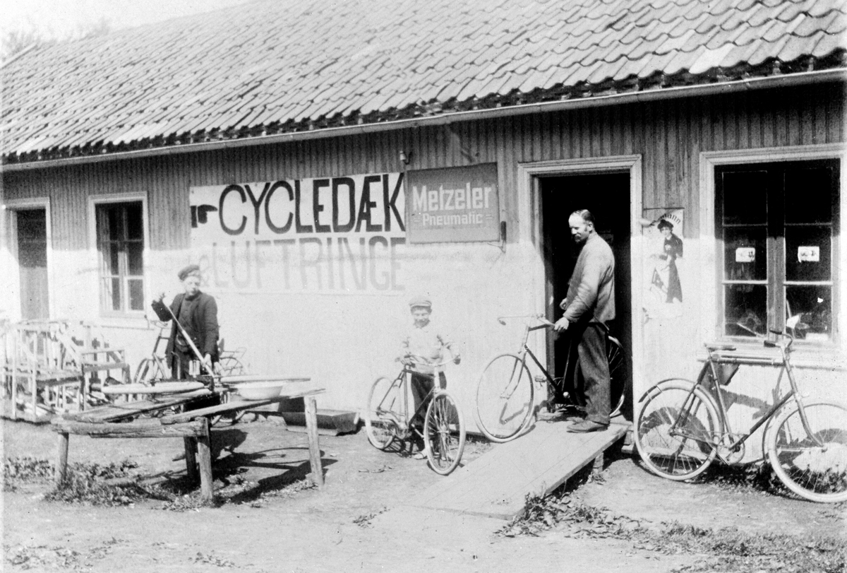 Anno Domkirkeodden, EKSTERIØR: BÆKKEVOLD SYKKELVERKSTED, "CYCLEDÆK LUFTRINGE" PÅ PLAKAT, GRUPPE:3 FORAN: FRANTZ EMERICH, ANDREAS BÆKKEVOLD, THEODOR BÆKKELUND, Løvstad G. nr. 7 b. nr. 4