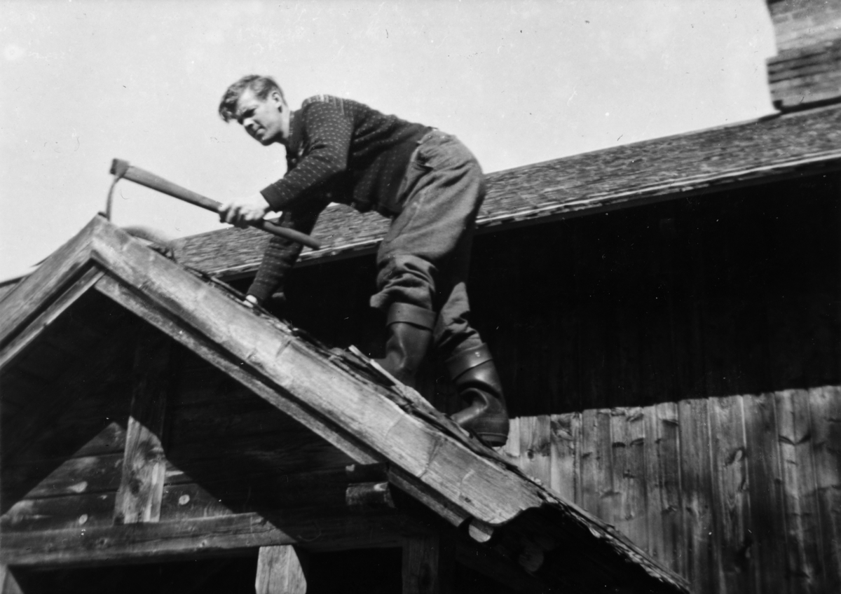 Ukjent, Fossengen nordre i Vallset ca. 1937-1938. Flistak var det mange steder den tida. De holdt kanskje i 15-20 år. Her har det gjort i fra seg og det gamle rives av med grev. Hustaket har alt fått ny flis- her står gangtaket for tur. Oskar lier bruker grevet.