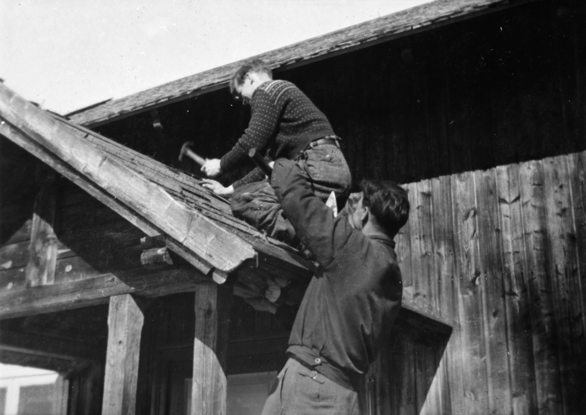 Ukjent, Fossengen nordre i Vallset ca. 1937-1938. Flistak var det mange steder den tida. De holdt kanskje i 15-20 år. Her har det gjort i fra seg og det legges nytt tak. Oskar Lier spikrer og broren Ingvar Lier hjelper til.