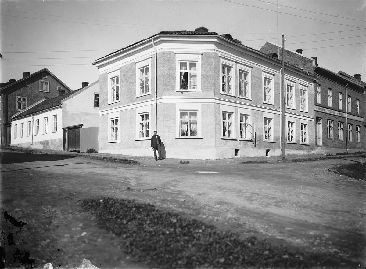 Oscar Løberg, Skappelsgate 1. Skappelsgården i krysset Skappelsgate, Morterudsgate, Hamar. Eksteriør. T.h. Oplandets Trykkeri &kontor. 1913-14, Elise Sandberg Knutsen sittende i vindu i 2. etg, foran: malermester Simen Knutsen, Skappelsgate 1, Hamar. Gården tilhørte maler Knutsen. Se 0401-01513 for hvordan bebyg…