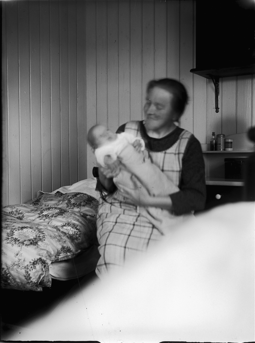 Ole M Martinsen, Ukjent kvinne holder et lite barn. Interiør, soverom, seng.
