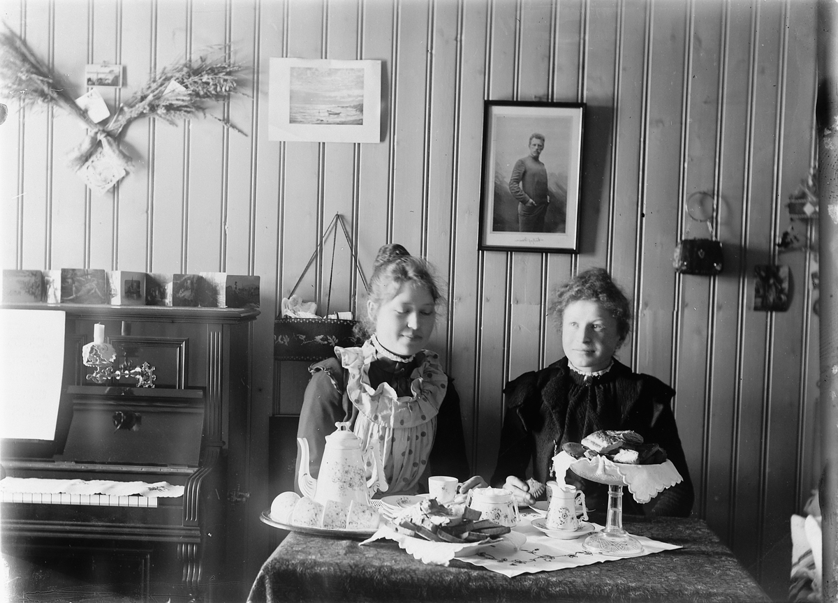 Mina Skraastad, Interiør, stue med piano. To kvinner drikker kaffe rundt et stuebord.