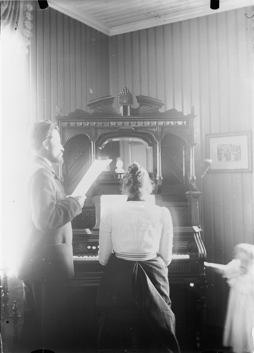 Mina Skraastad, Interiør, stue med orgel. En mann synger og ei kvinne spiller.