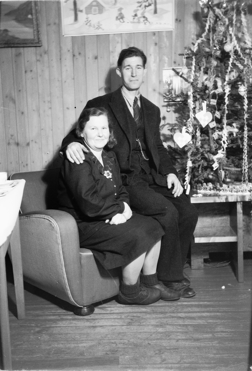 Håkon Prestkværn, Interiør, stue. Sparemøte, Syvertsen. Ukjent kvinne og mann foran juletre.