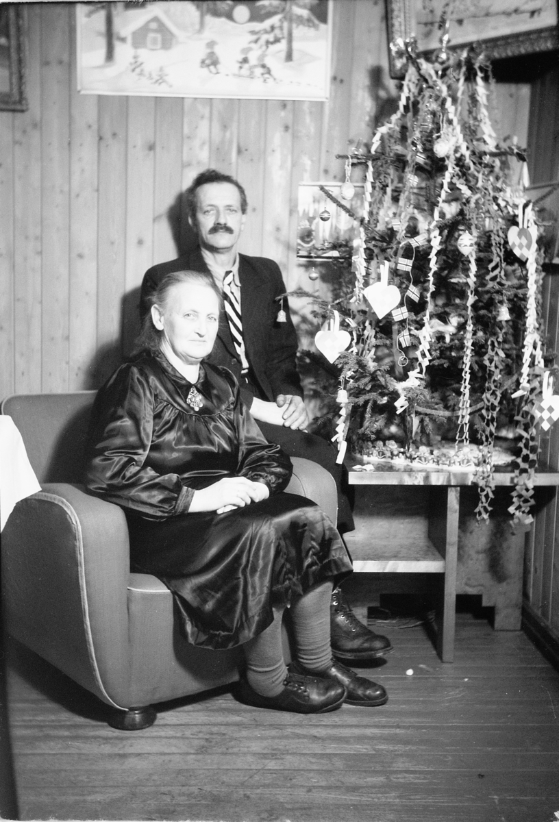 Håkon Prestkværn, Interiør, stue. Sparemøte, Syvertsen. Ukjent kvinne og mann foran juletre.