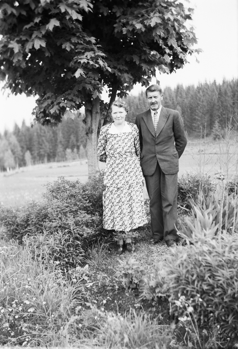 Håkon Prestkværn, Ukjent kvinne og mann i en hage med jorde og skog i bakgrunnen.