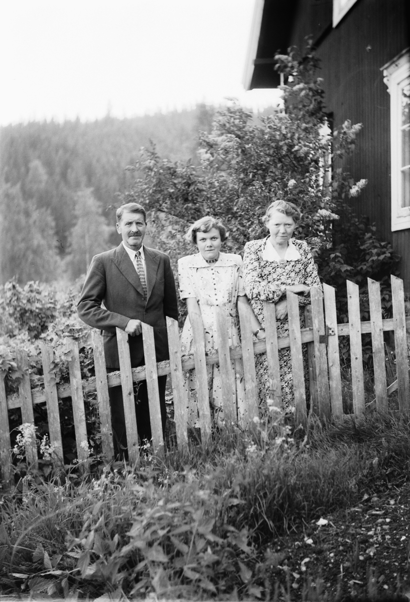 Håkon Prestkværn, Ukjent mann og to kvinner i hage ved gjerde.