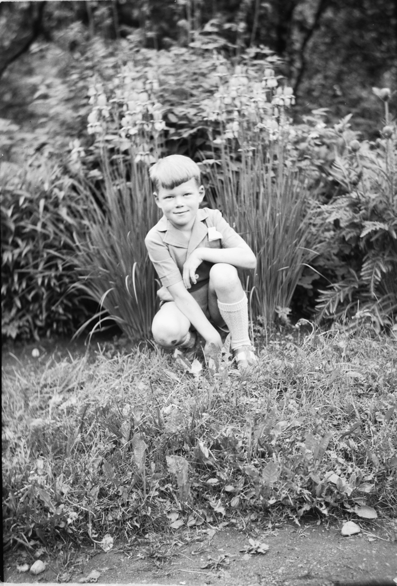Håkon Prestkværn, Knut Haug, f. 1944, sitter på huk i en hage.