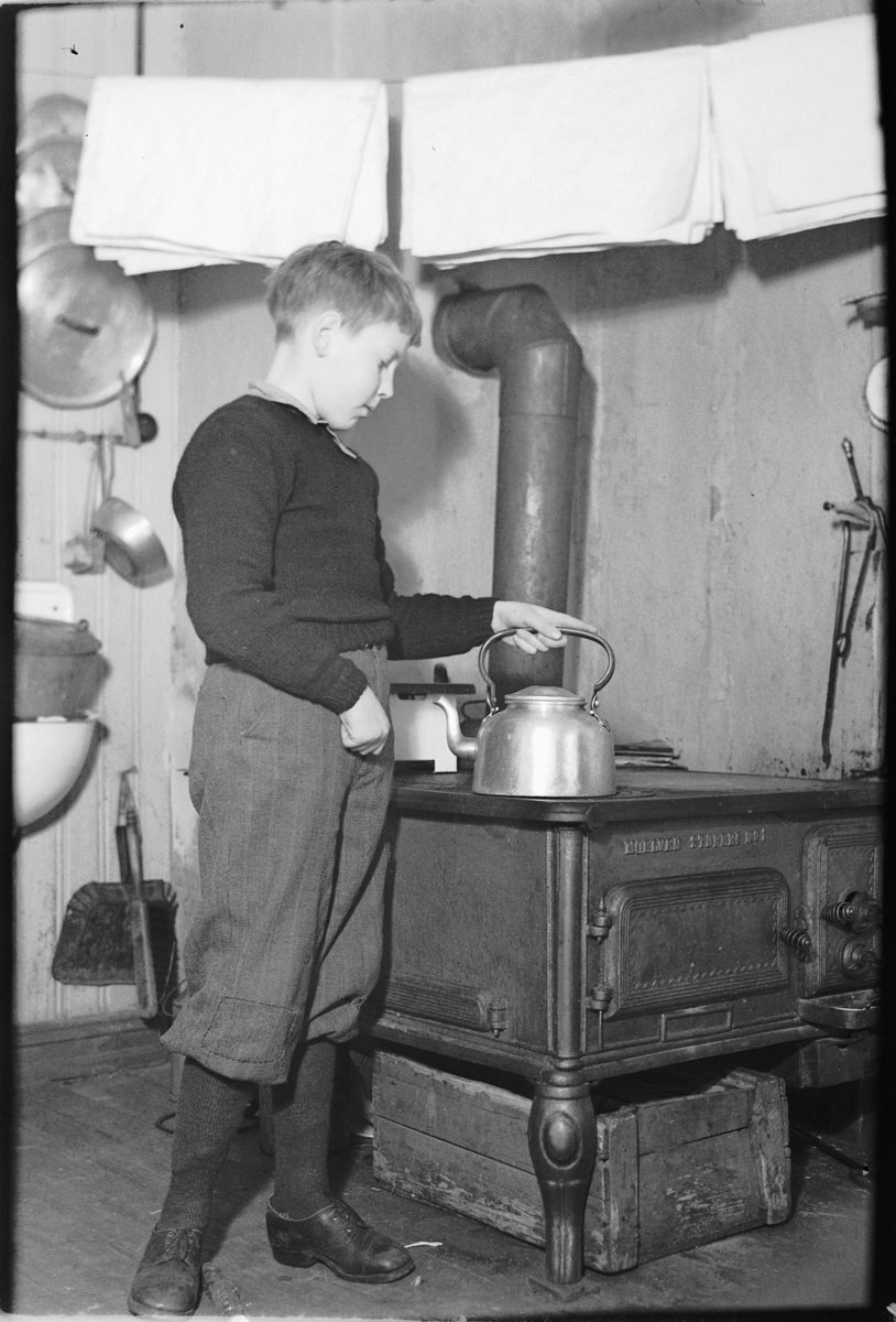 Håkon Prestkværn, Ole Christian Prestkværn (11 år gammel) koker kaffe på ovn, komfyr produsert ved Moelv støperi. Interiør fra kjøkkenet på Løkkekværn Gård, Moelv.