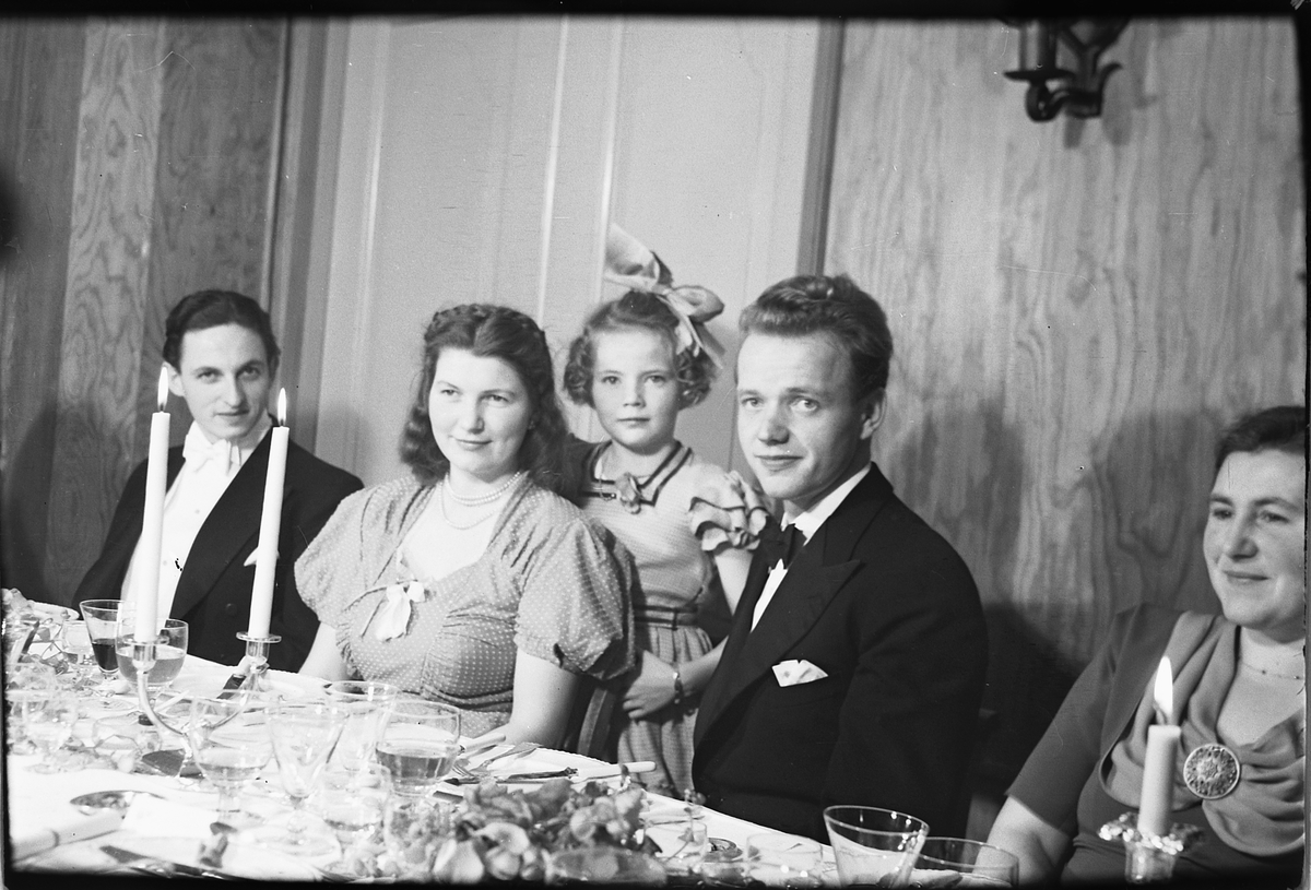 Håkon Prestkværn, Arendal, sølvbryllup. Ukjente personer ved pyntet bord, pike med sløyfe. Fotokonvolutten mrk. "Bryll. Enger Tjerne(?) okt 1951"