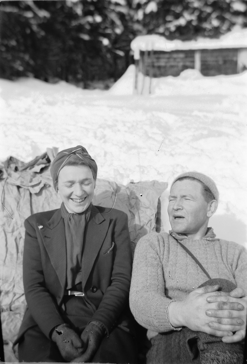 Håkon Prestkværn, Ukjent mann og kvinne sitter i snøen i skogen.
