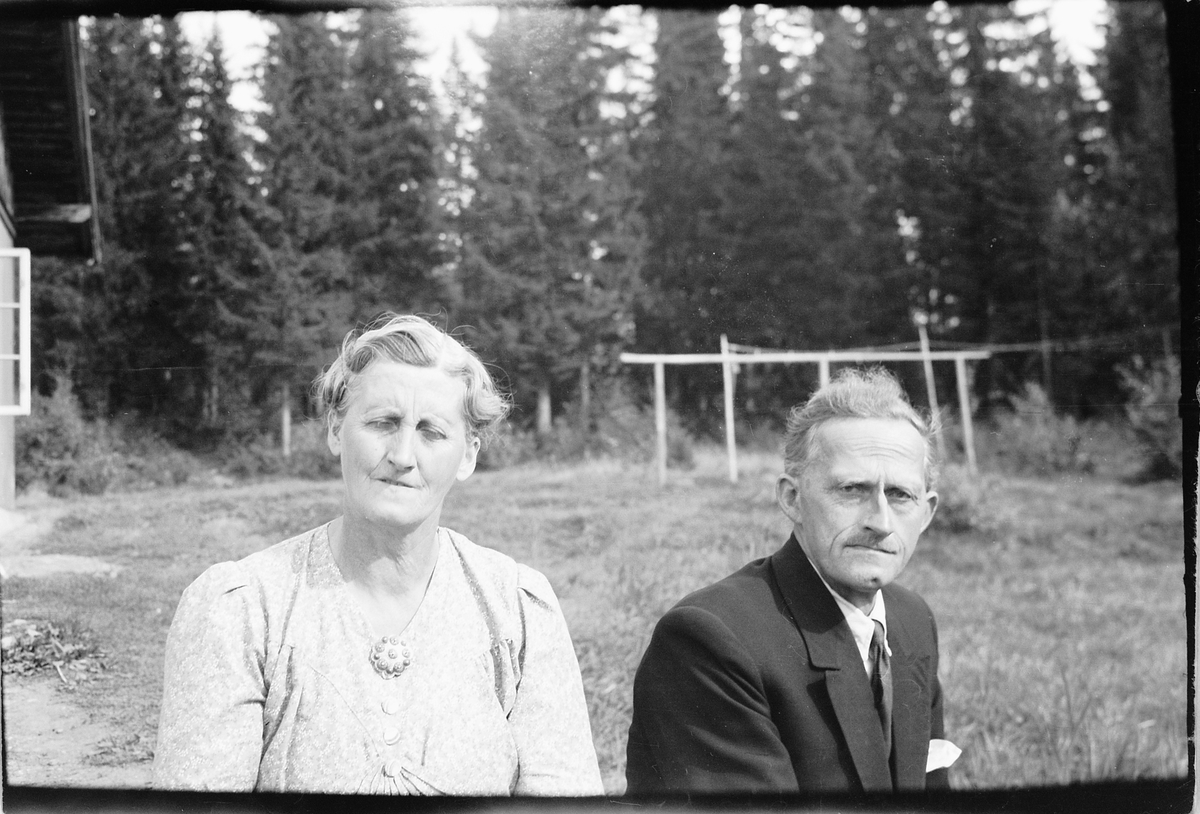 Håkon Prestkværn, Eldre mann og kvinne sitter ute ved et hus.
