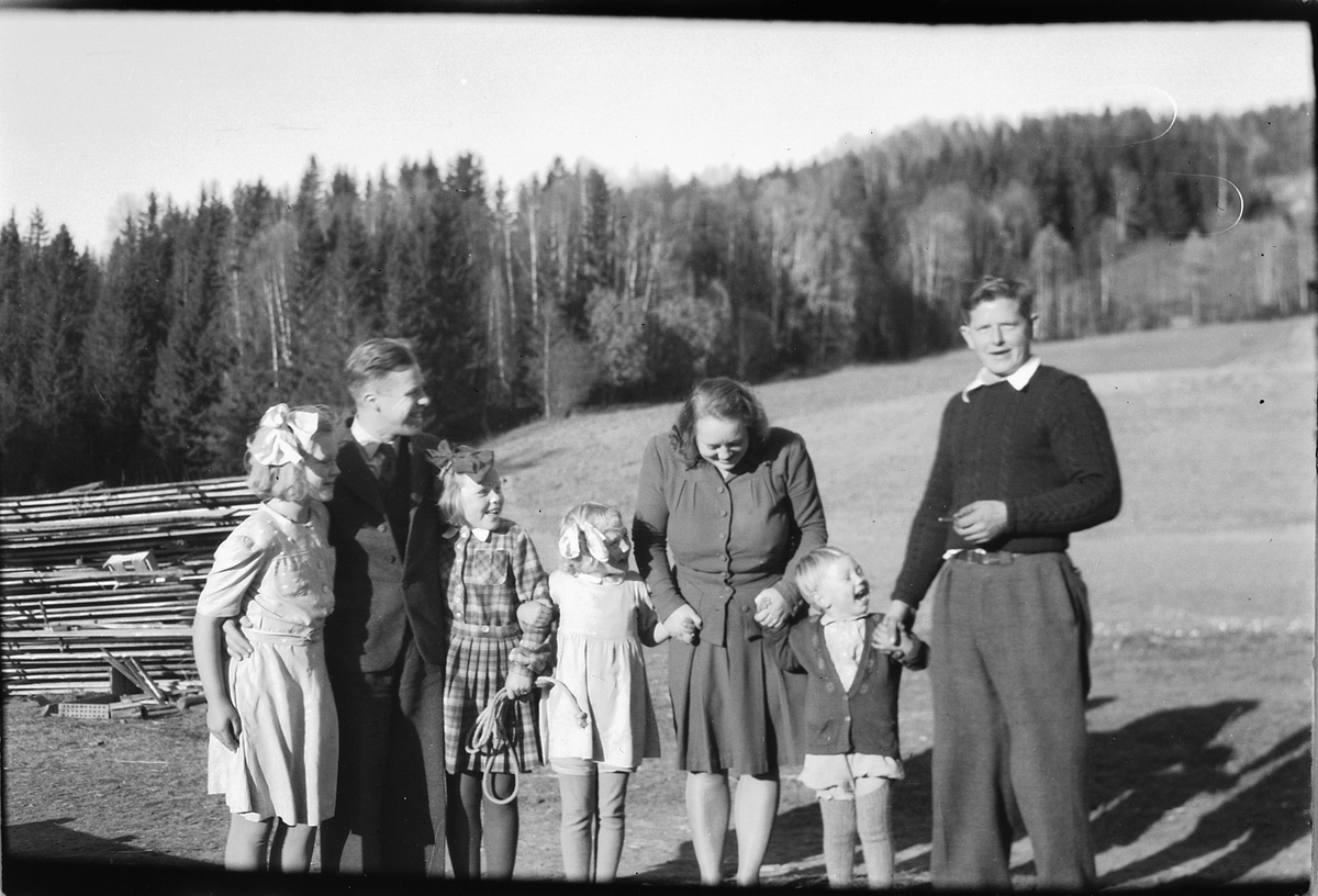 Håkon Prestkværn, Ukjent kvinne sammen med to menn og tre barn foran en plankestabel og et jorde.