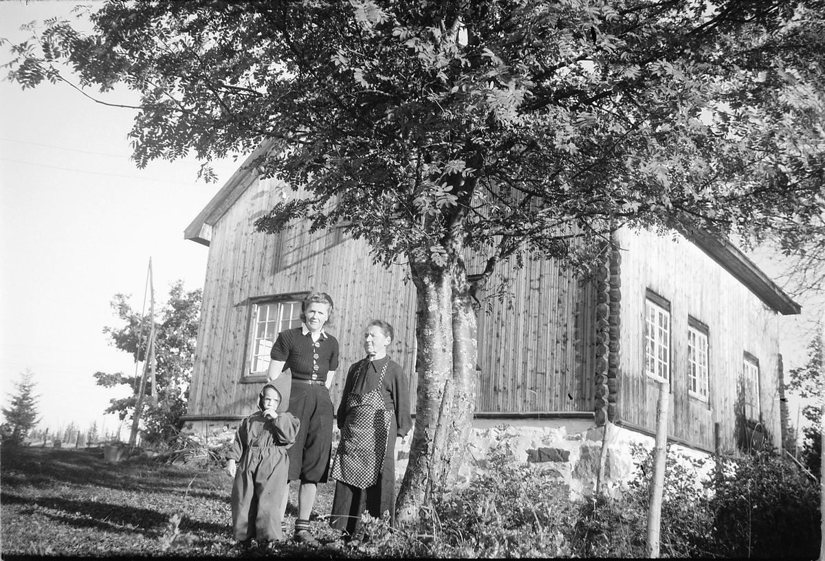 Håkon Prestkværn, To ukjente kvinner med et barn foran et hus.