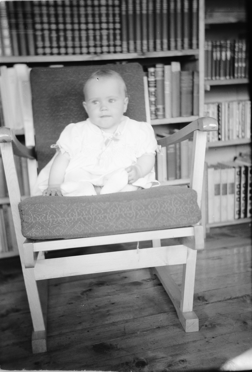 Håkon Prestkværn, En baby sitter i en stol foran en bokhylle.