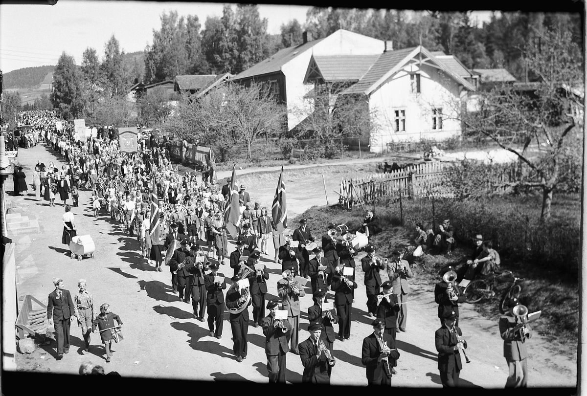 Håkon Prestkværn, 17. -MAI-TOG I MOELV, STORGATA MED HUSET TIL WIEN I BAKGRUNNEN, FORAN LENSMANN BULL I HVIT UNIFORM, NORSKE FLAGG, BARNETOG.