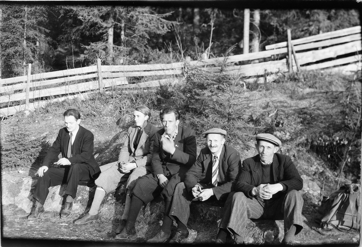 Håkon Prestkværn, Gruppe menn sitter og hviler på en stein med et gjerde i bakgrunnen.