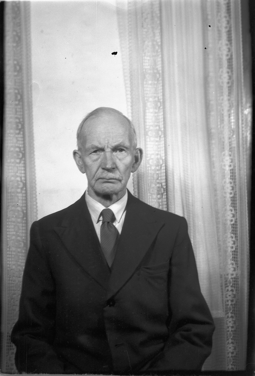 Håkon Prestkværn, Eldre mann foran vindu med gardiner.