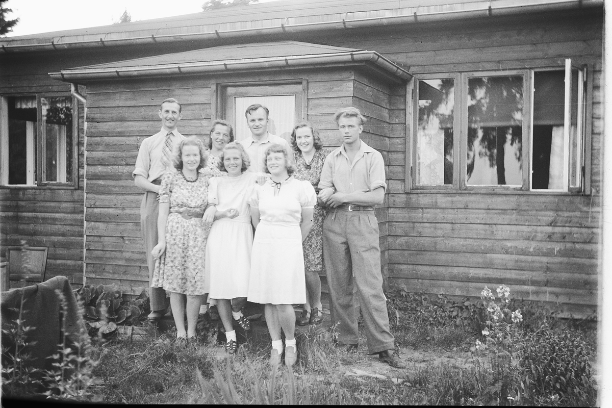 Håkon Prestkværn, Ukjent gruppe 5 kvinner og 3 menn ved inngangspartiet til hus / hytte. Midt foran inngangsdøra står Harald Kolltveit