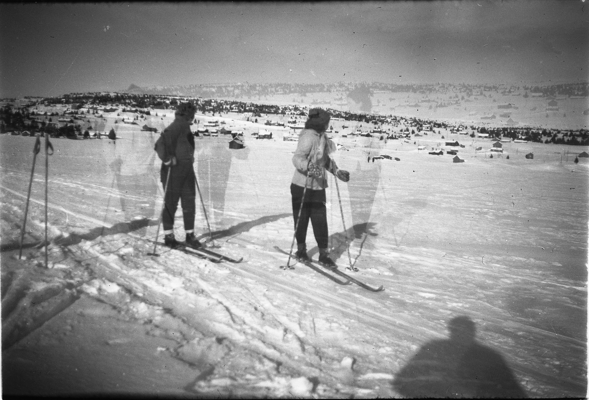 Håkon Prestkværn, Vinterlandskap på fjellet med hyttefelt i bakgrunnen. To skigåere nyter utsikten.