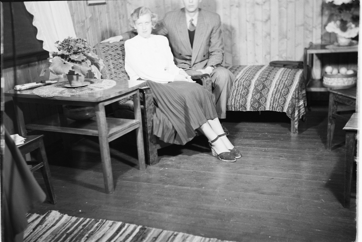 Håkon Prestkværn, Interiør, stue. Ukjent kvinne i stol og en mann i sofaen.