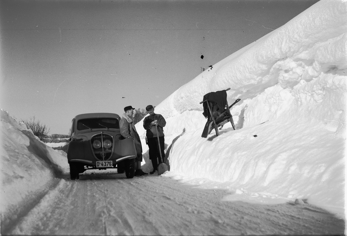 Håkon Prestkværn, Bil og to menn på en vintervei med brøytekanter. Vegoppsynsmann i nordre Ringsaker i samtale med vegvokter. Brøttum. Bilen er en Peugeot reg. nr. D-4376. Februar 1951. Snøvinter.
