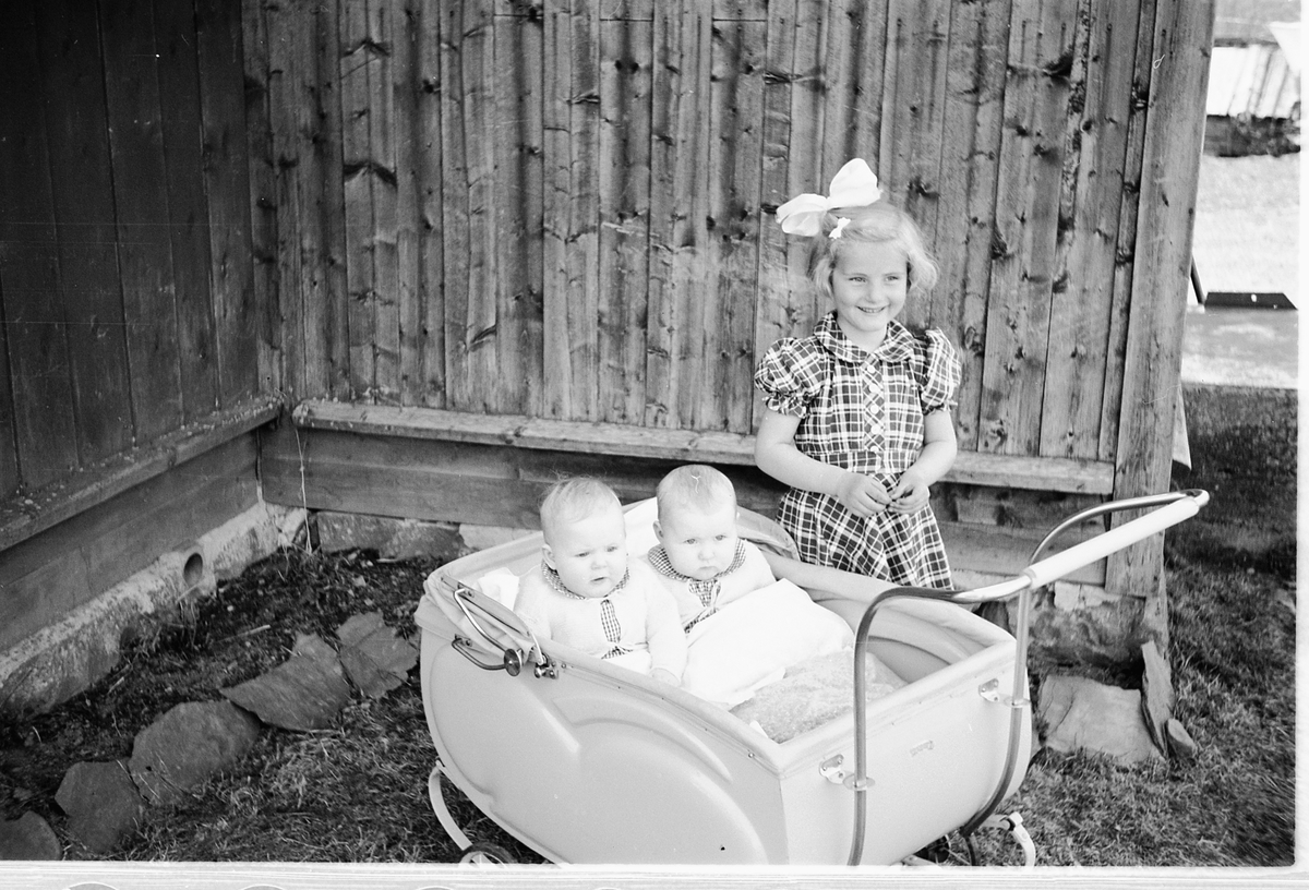Håkon Prestkværn, Tvillingene i vogna er Knut og Bjørg Svenskerud f. 1949. Jenta med sløyfe er Inger Svenskerud f. 1945. Bildet er tatt ved Åsmarka kirkestue. Jente med sløyfe i håret og to babyer i barnevogn.