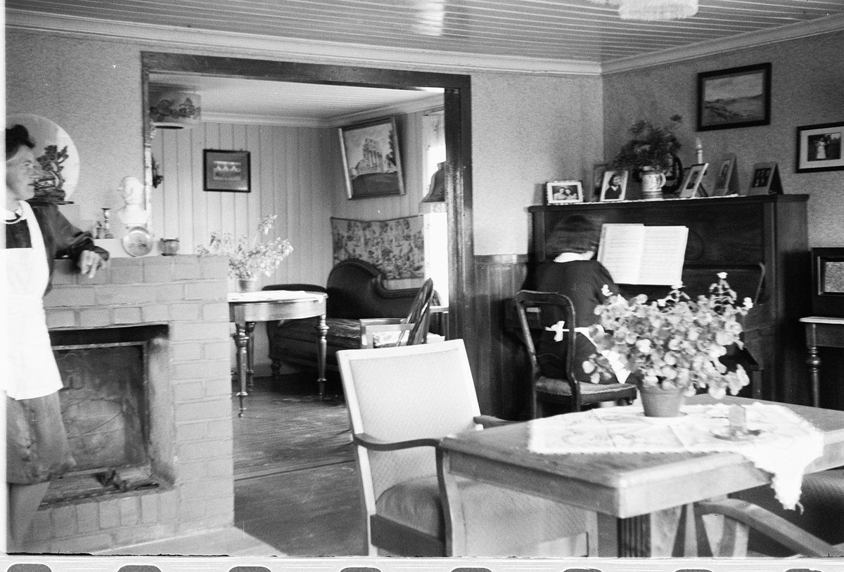 Håkon Prestkværn, Interiør, stue. Kvinne spiller piano.