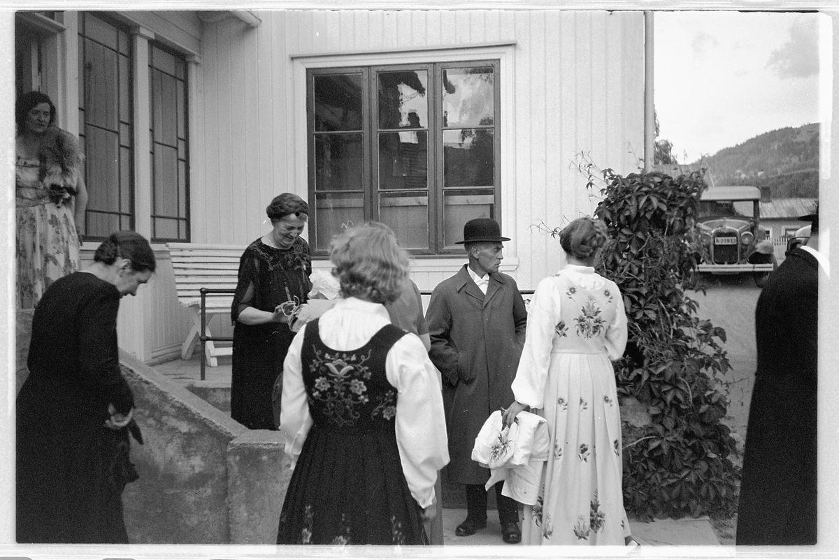 Håkon Prestkværn, Eksteriør, Brumunddal hotell. Gruppe kvinner med kjoler og bunad, en mann med frakk og hatt.